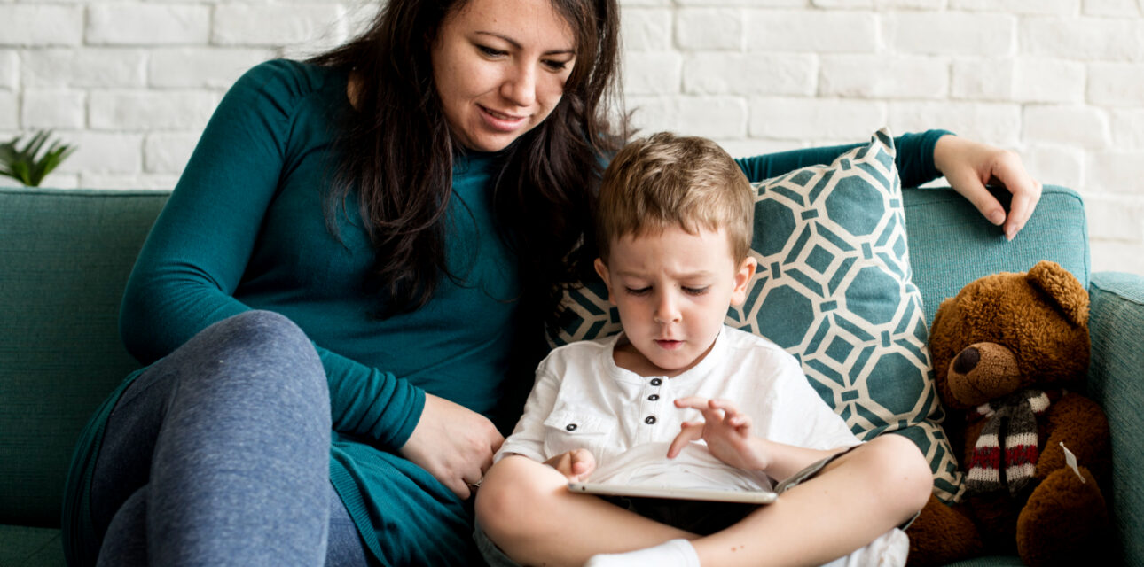 BCBA sitting with autistic child using a tablet on the couch.
