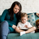 BCBA sitting with autistic child using a tablet on the couch.