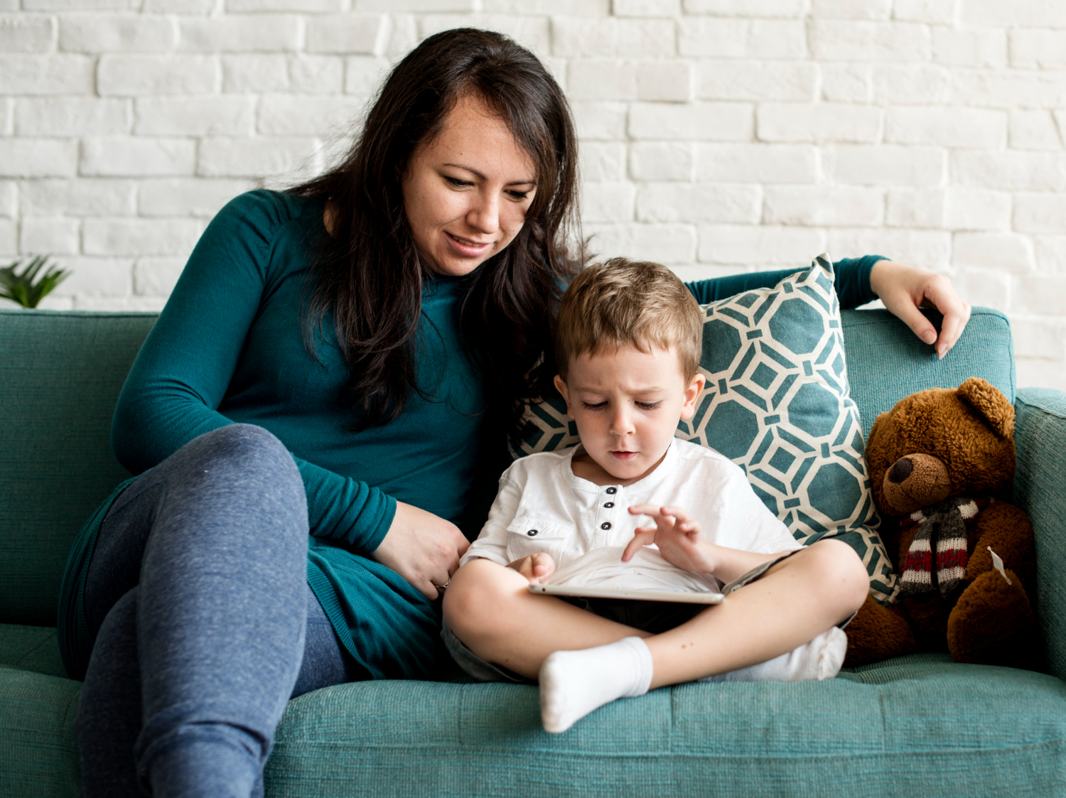 BCBA sitting with autistic child using a tablet on the couch.