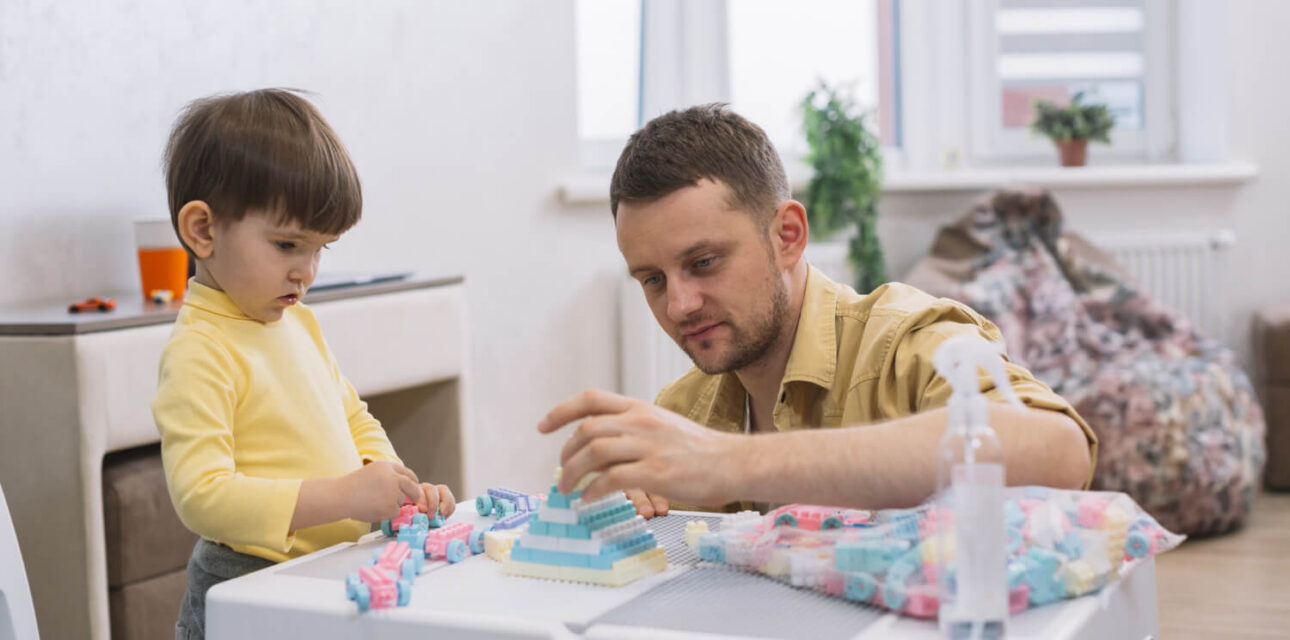 ABA therapist helping a young child build with blocks during a play-based therapy session.