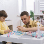 ABA therapist helping a young child build with blocks during a play-based therapy session.