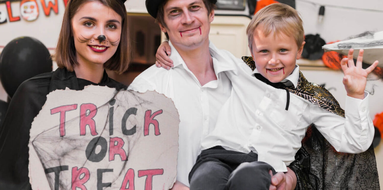 Family dressed in Halloween costumes holds a trick-or-treat sign.
