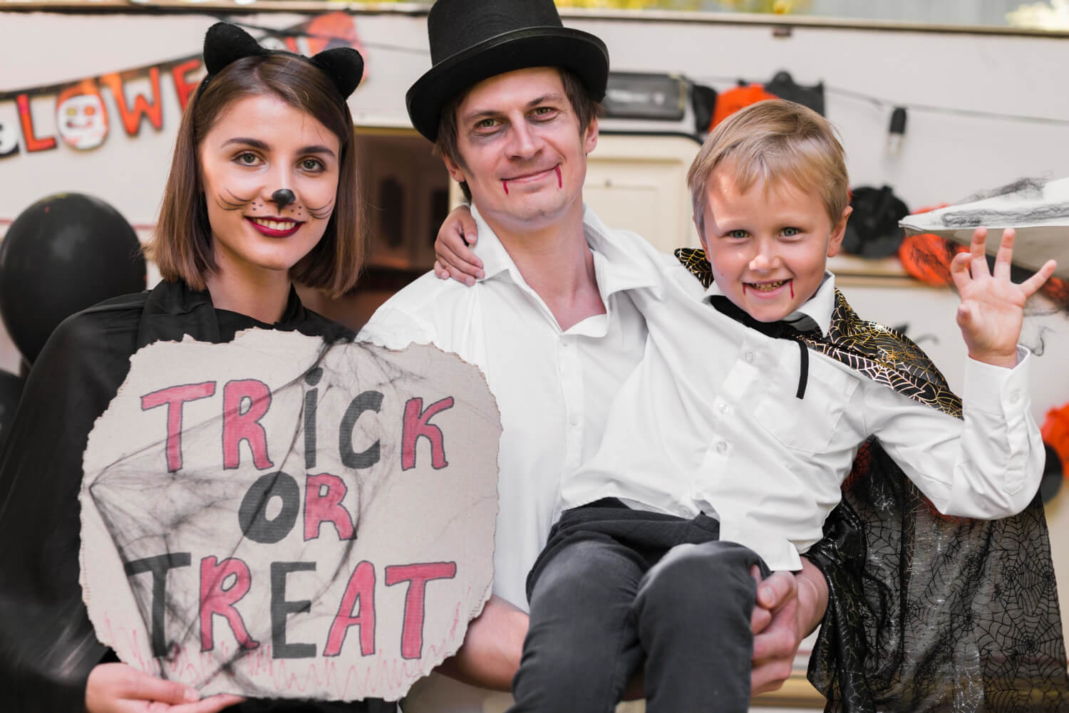 Family dressed in Halloween costumes holds a trick-or-treat sign.