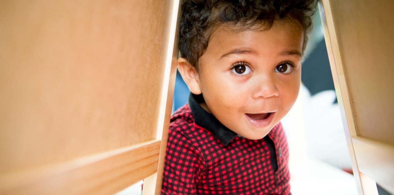 Young child peeking through a play structure during an autism-related activity.