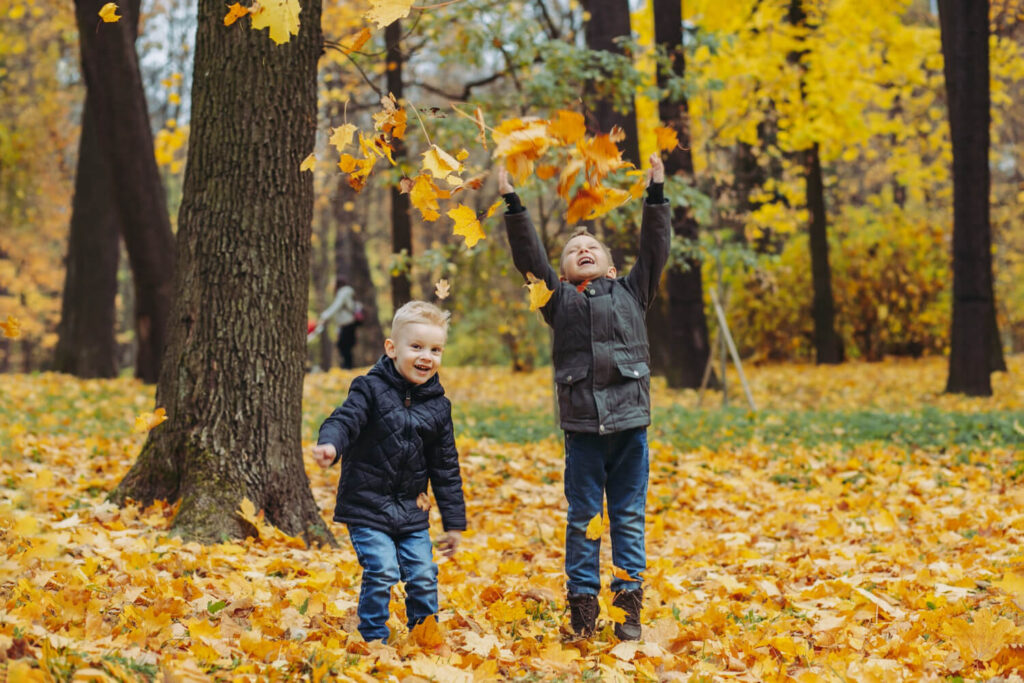 Two children with autism enjoying a sensory-friendly fall outing while playing in autumn leaves.
