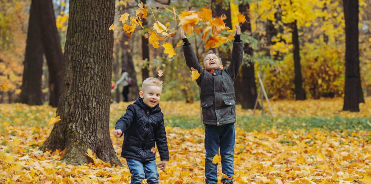 Two children with autism enjoying a sensory-friendly fall outing while playing in autumn leaves.