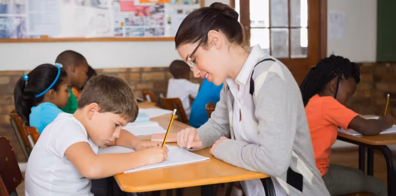 Teacher providing one-on-one school-based ABA support to a student with autism during a classroom writing activity.