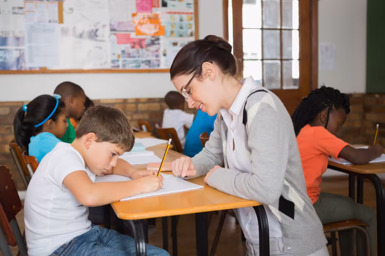 Teacher providing one-on-one school-based ABA support to a student with autism during a classroom writing activity.