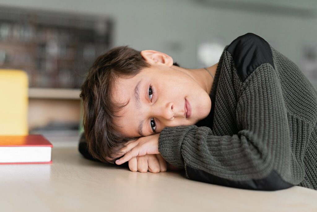 Young boy with autism resting his head on his arms at a classroom table.