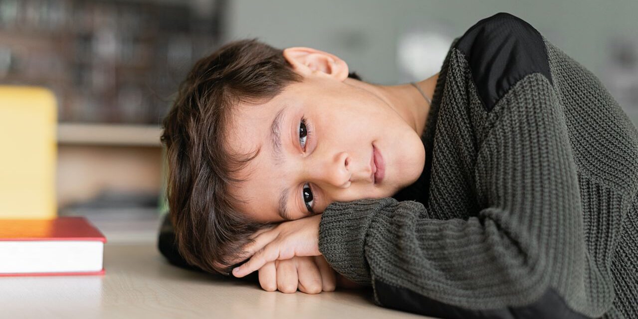 Young boy with autism resting his head on his arms at a classroom table.