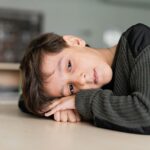 Young boy with autism resting his head on his arms at a classroom table.