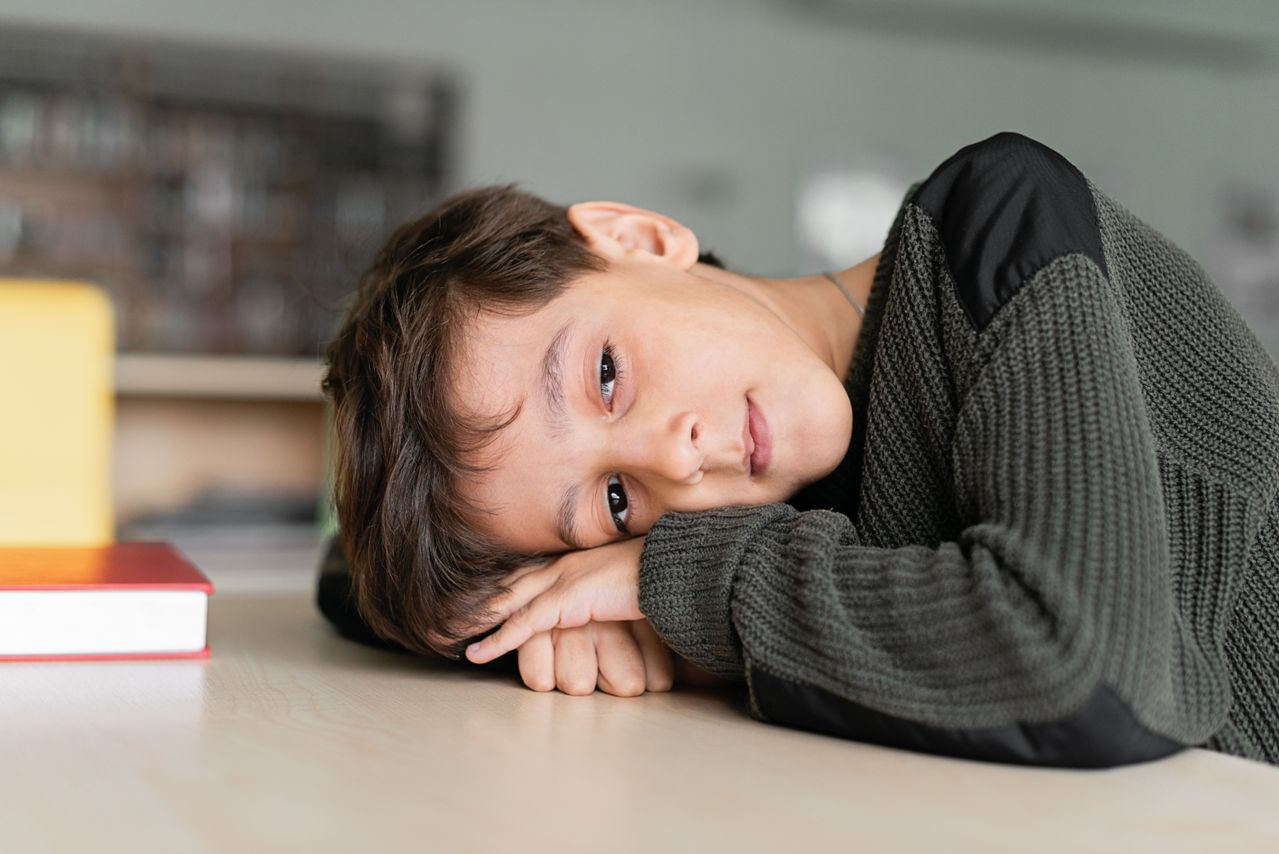Young boy with autism resting his head on his arms at a classroom table.