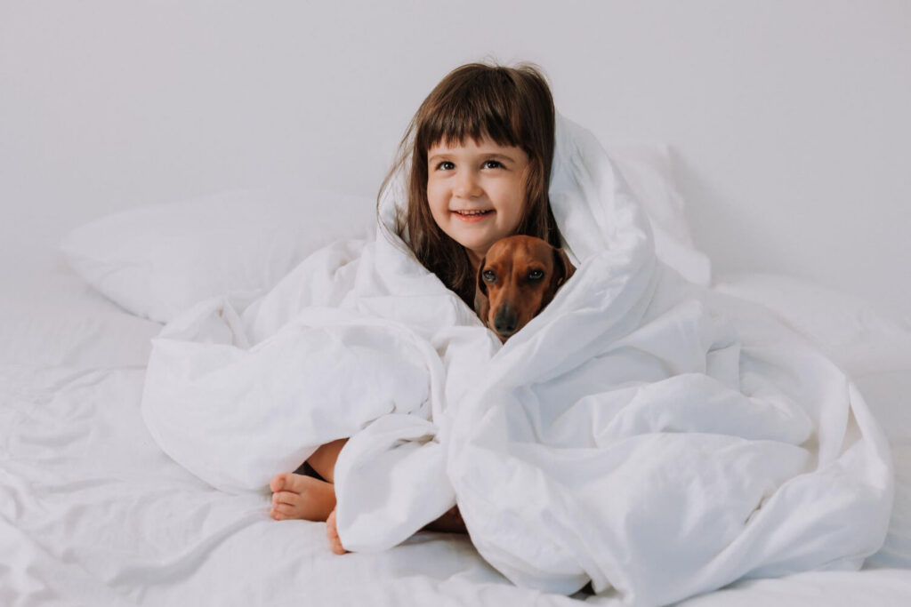 Child cuddling with a dog under a blanket, illustrating weighted blankets for autistic children.