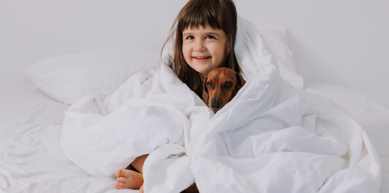 Child cuddling with a dog under a blanket, illustrating weighted blankets for autistic children.