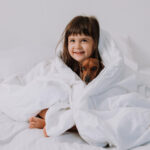 Child cuddling with a dog under a blanket, illustrating weighted blankets for autistic children.