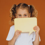 Young girl with autism holding a speech bubble card while learning to communicate.