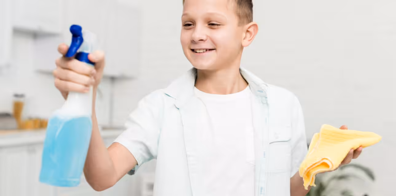 Smiling young boy holding cleaning supplies while learning household chores.