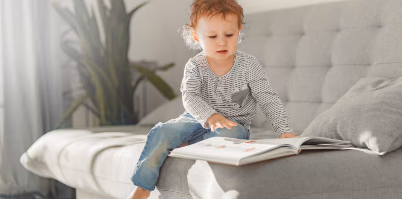 Young child with autism looking through a picture book while sitting on a couch.