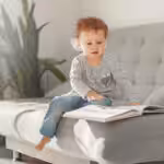 Young child with autism looking through a picture book while sitting on a couch.