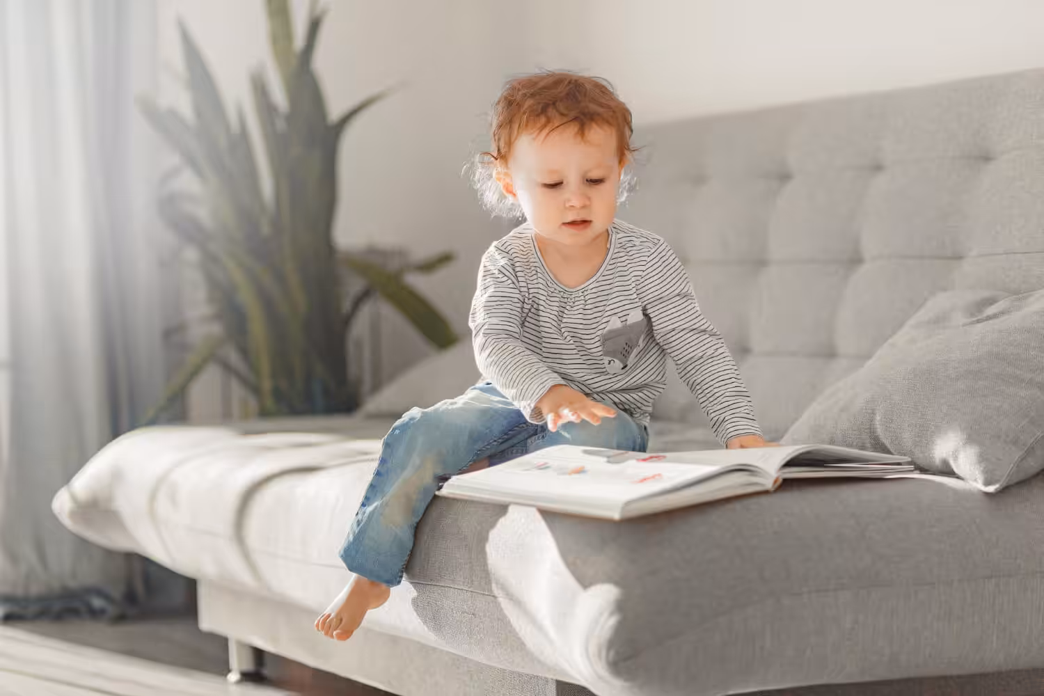 Young child with autism looking through a picture book while sitting on a couch.