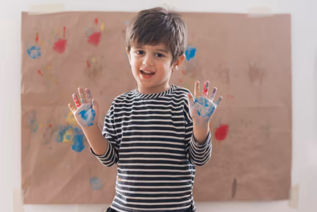 Smiling boy showing paint-covered hands.