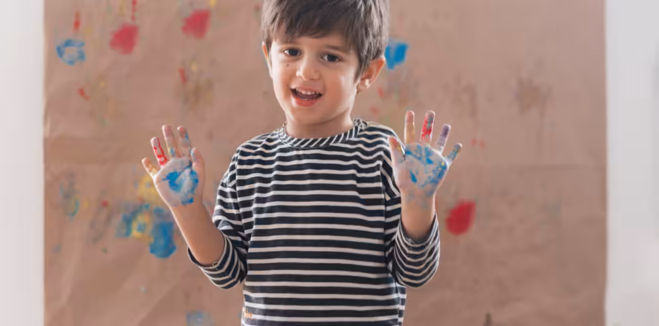Smiling boy showing paint-covered hands.