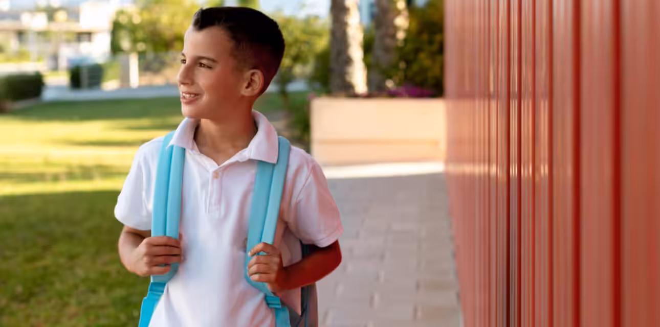 School-aged autistic boy with a backpack walking outside a school building.