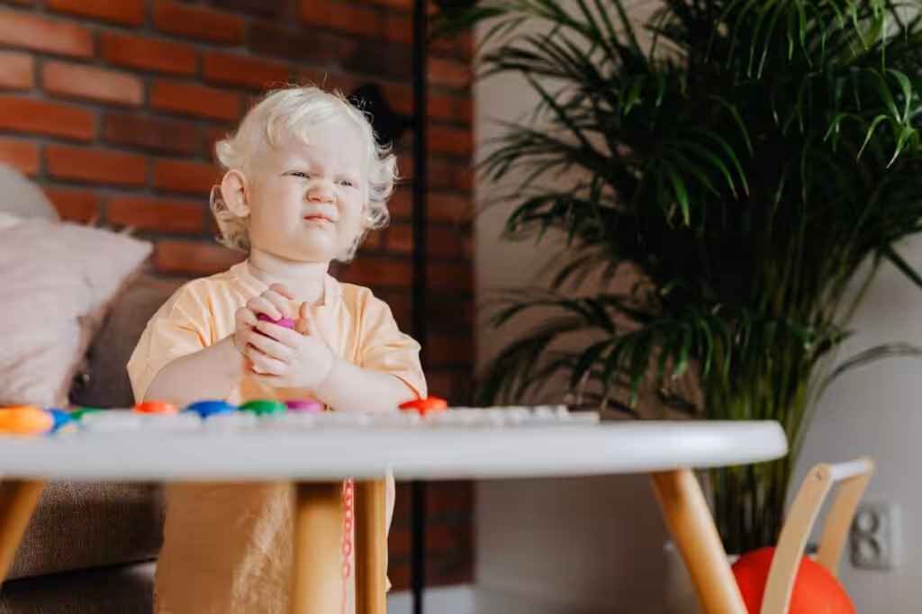 Frustrated toddler holding a toy while sitting at a table.