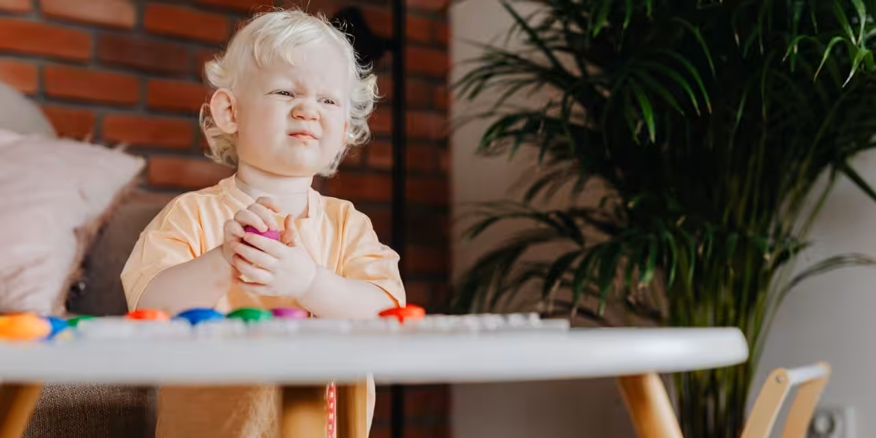 Frustrated toddler holding a toy while sitting at a table.
