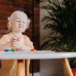 Frustrated toddler holding a toy while sitting at a table.